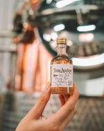 Hand holding a small bottle of Time Anchor Distillery bottle your own Gin infron t of a large copper pit still